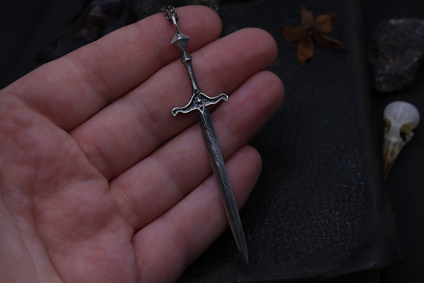 Silver sword-shaped pendant held in a hand with a dark background
