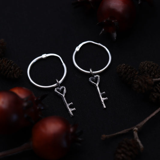 A pair of sterling silver earrings shaped like keys, displayed against a dark background with rustic elements.