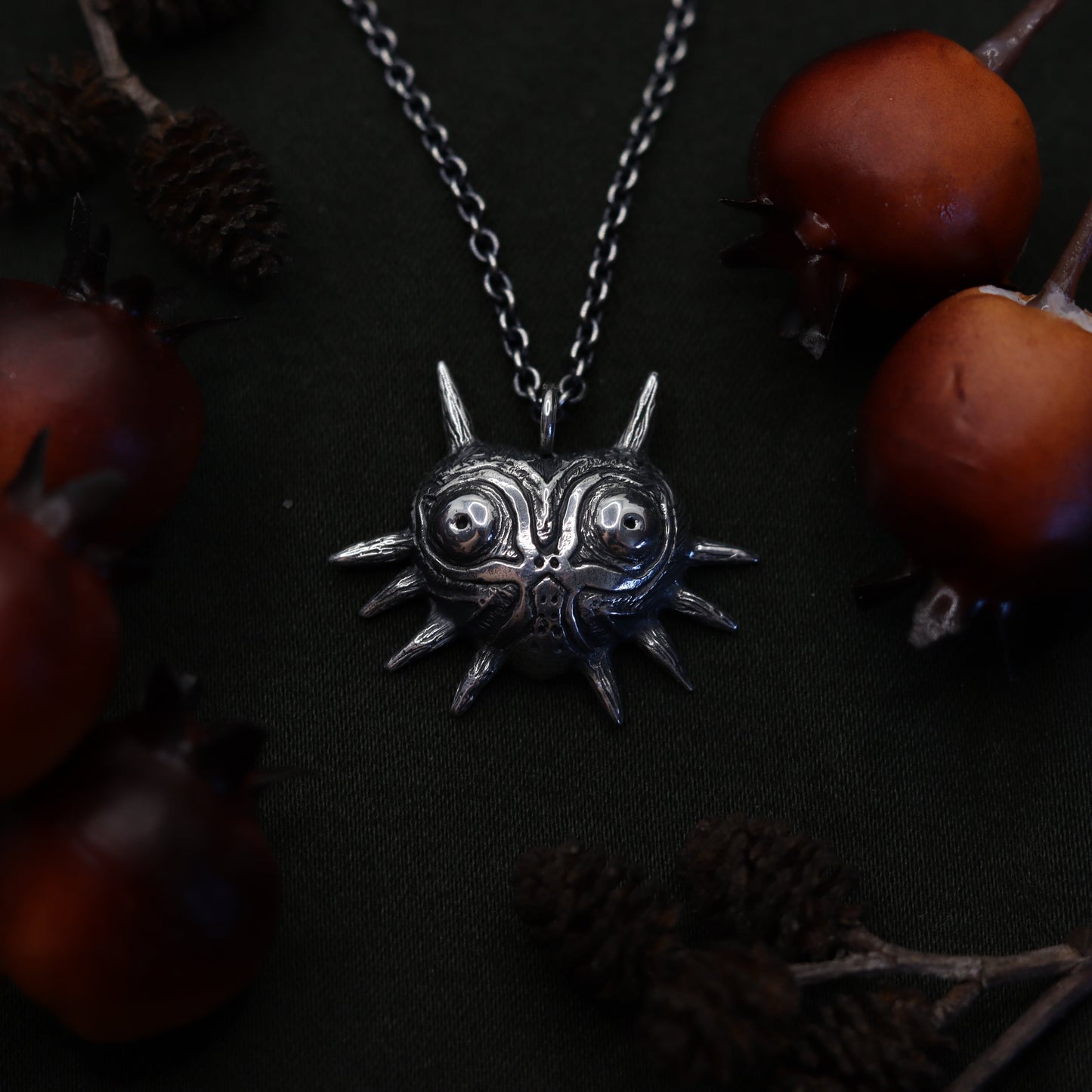 A necklace with a heart-shaped pendant resembling Majora's Mask from The Legend of Zelda series, displayed against a dark background