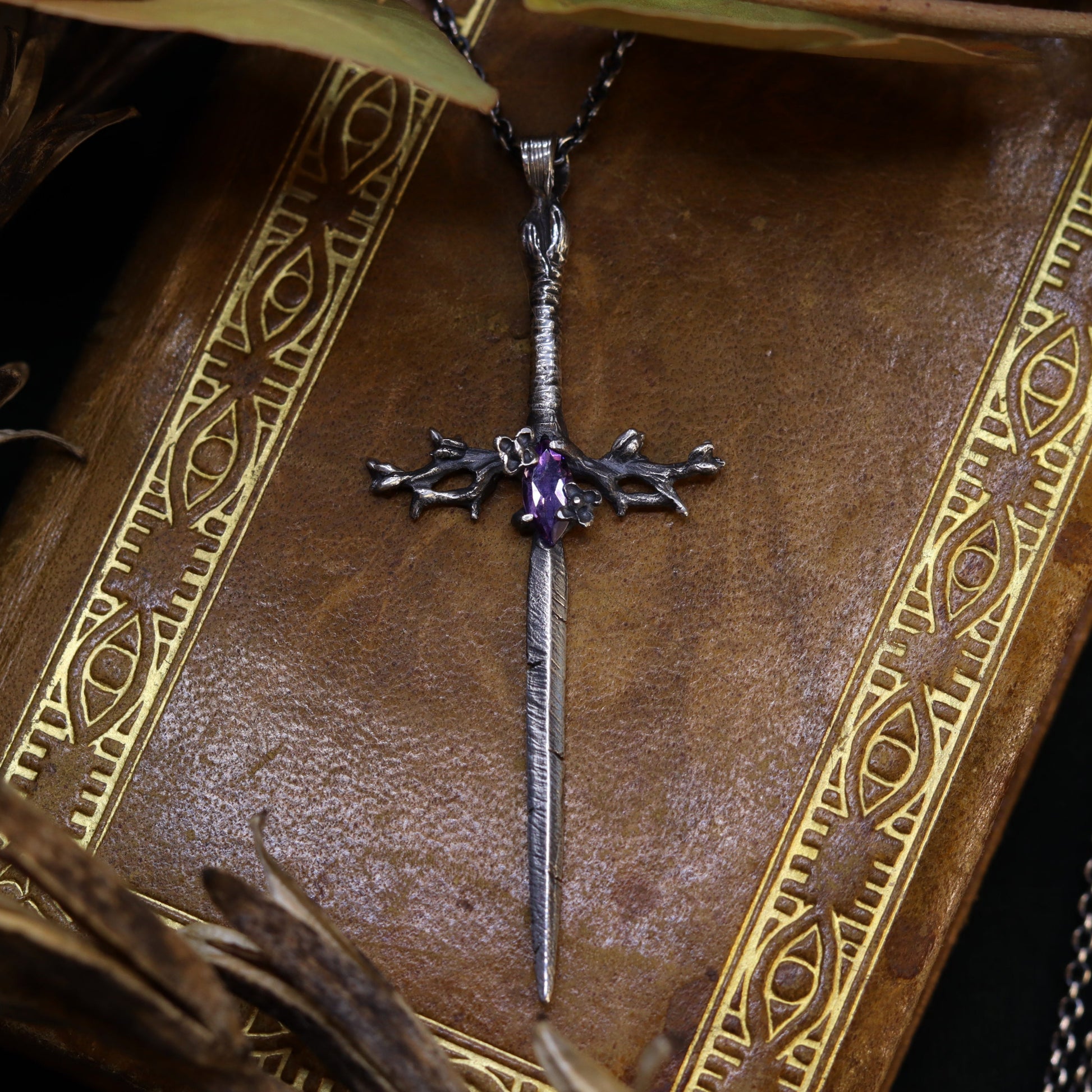 A delicate lilac sword-shaped necklace with an amethyst stone, displayed on a book.