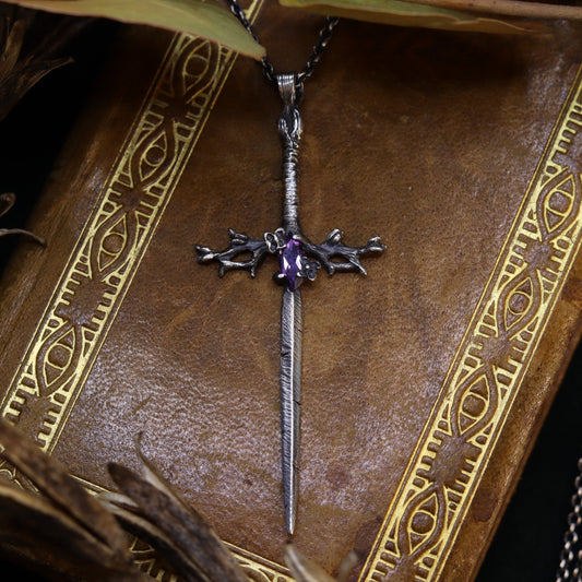 A delicate lilac sword-shaped necklace with an amethyst stone, displayed on a book.