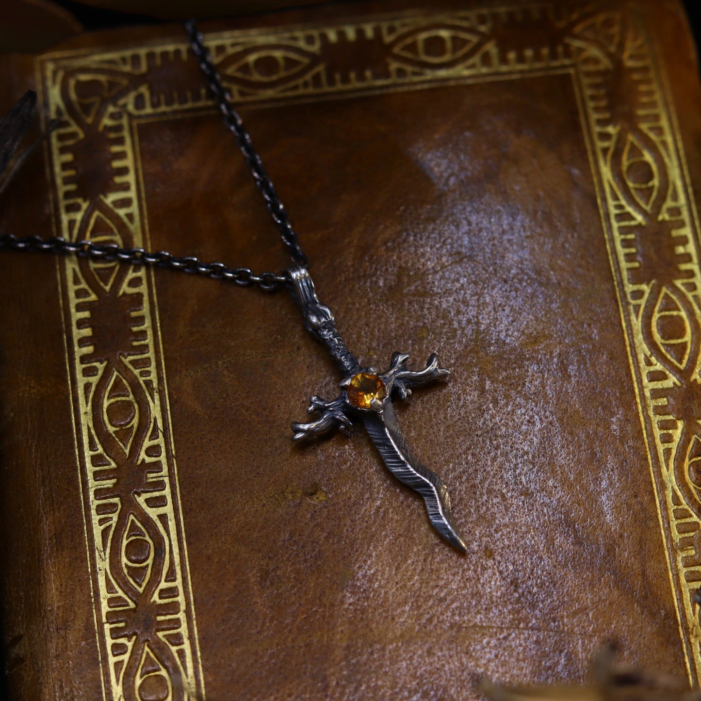 A silver necklace with a dagger-like design, featuring a radiant citrine stone, displayed on a book.