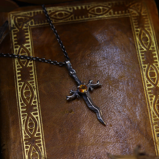 A silver necklace with a dagger-like design, featuring a radiant citrine stone, displayed on a book.