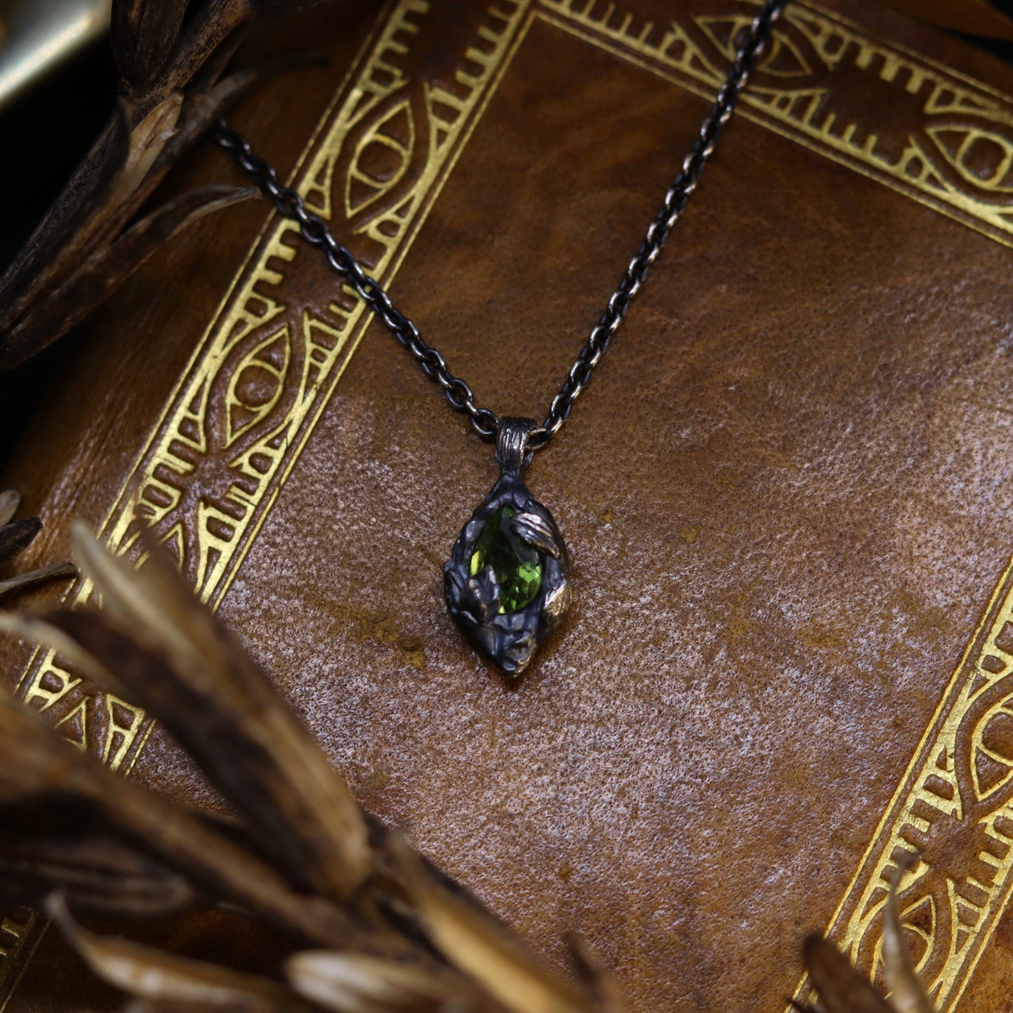 A necklace with a sterling silver pendant featuring a peridot stone at its core, surrounded by small leaf details, displayed on a textured background.