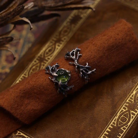 A silver ring with an antler-shaped design, set with a peridot stone, displayed on a brown textured surface.