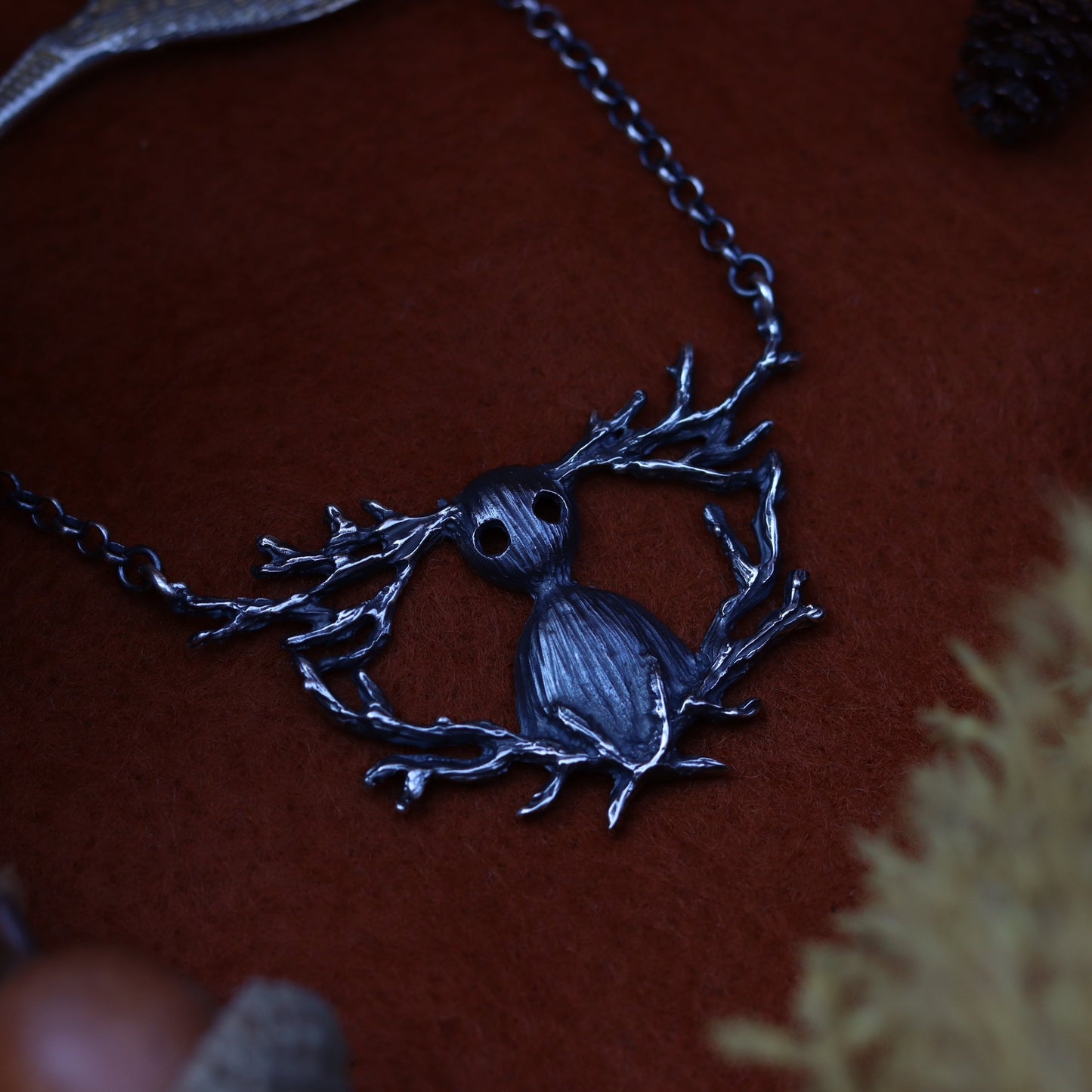 A Sterling silver necklace with a unique design, featuring a character inspired by 'Over The Garden Wall' placed on a red surface with autumn leaves around it.