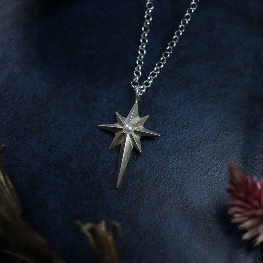 A sterling silver necklace with a star-shaped pendant and a pearl in the center, displayed on a dark background