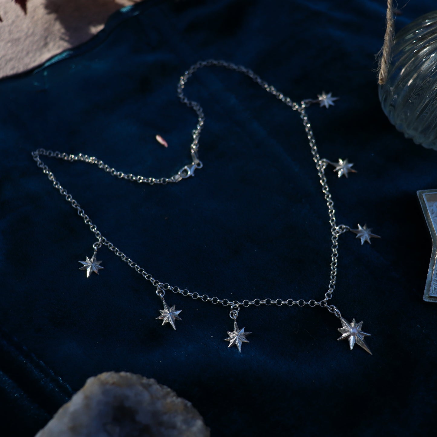 A sterling silver necklace with a central pearl star, surrounded by smaller star designs, displayed on a blue velvet surface.