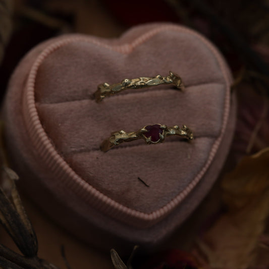 Two gold rings with red ruby are displayed on a heart-shaped cushion.