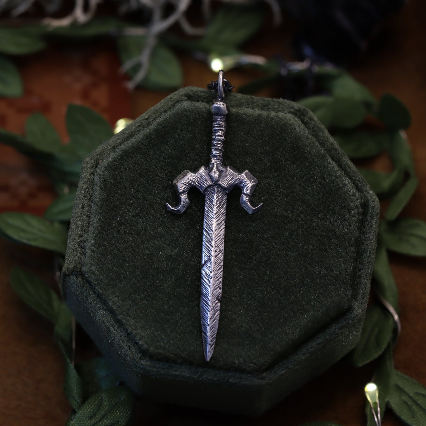 A necklace pendant designed to resemble the Galaxy Sword from the video game Stardew Valley, displayed on a dark, fabric-wrapped stand.