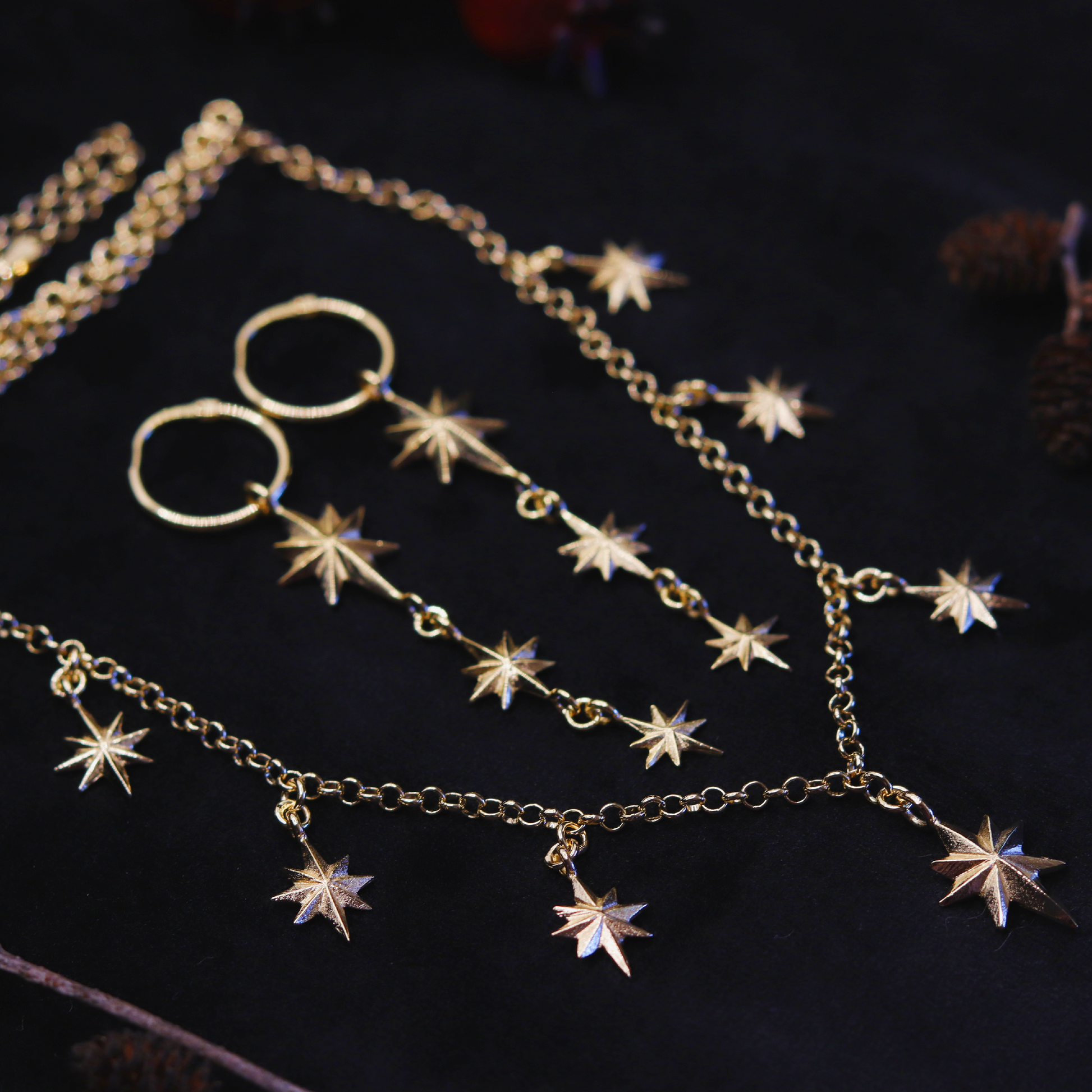 A gold plated necklace with star-shaped pendants, displayed against a dark fabric background.