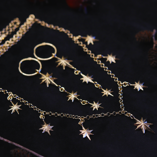 A gold plated necklace with star-shaped pendants, displayed against a dark fabric background.