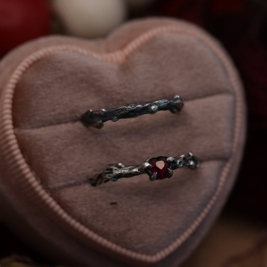 A heart-shaped ring box containing a silver ring with a red ruby.