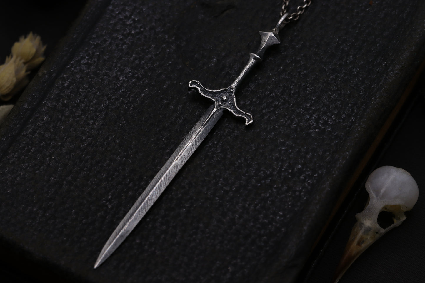 Silver sword-shaped pendant on a dark textured surface