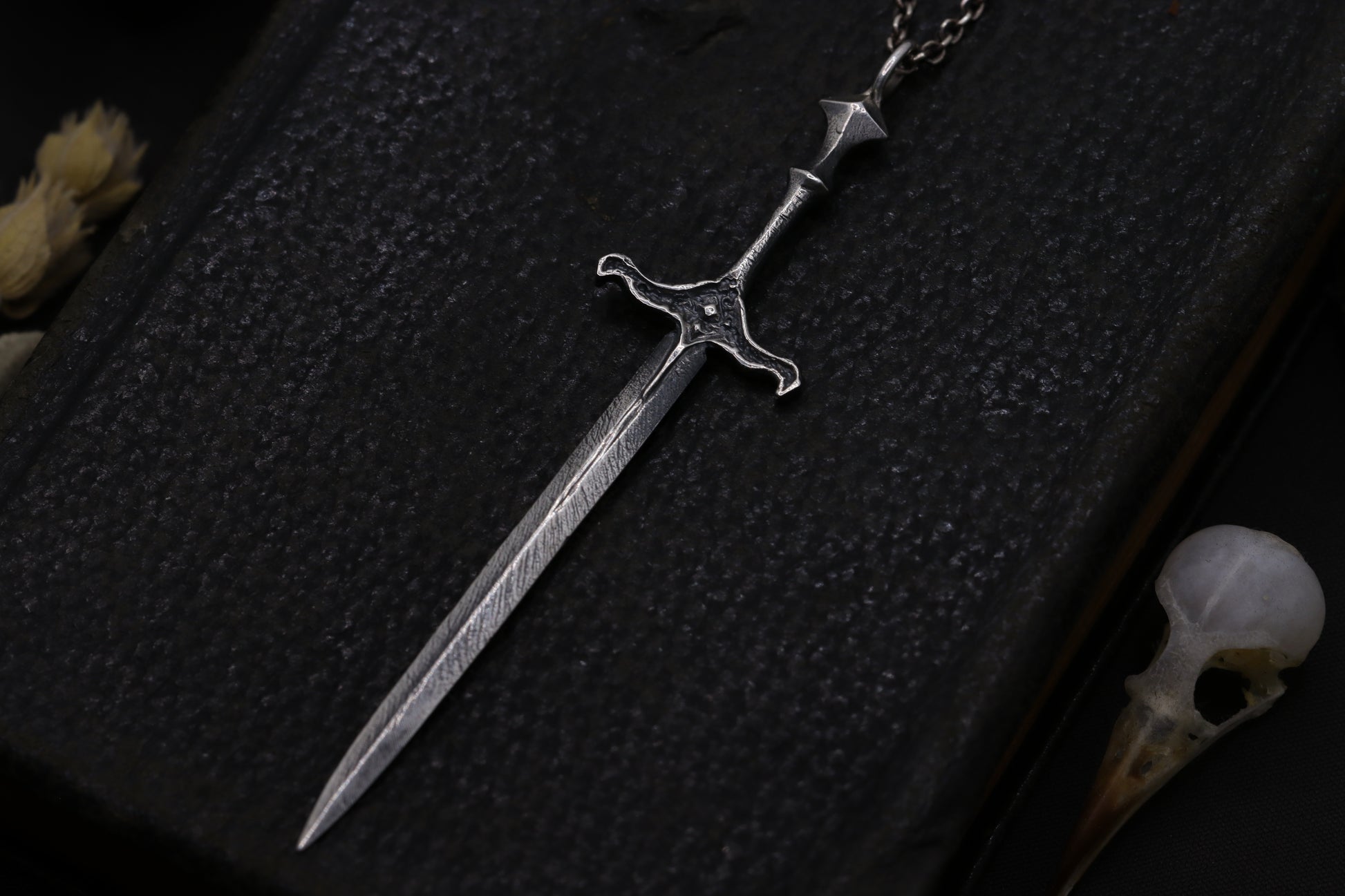 Silver sword-shaped pendant on a dark textured surface