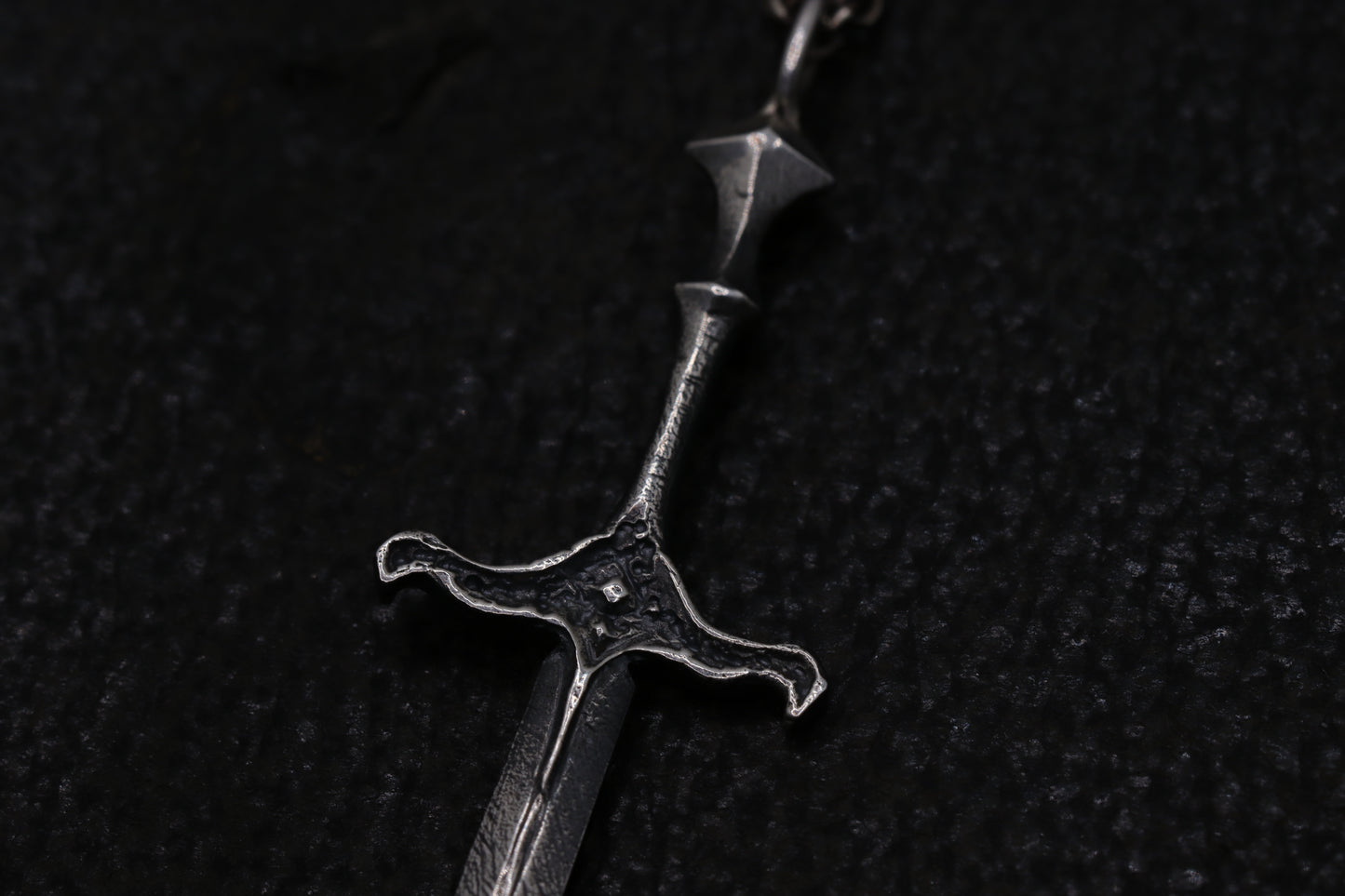 Close-up of a silver sword pendant on a dark textured background