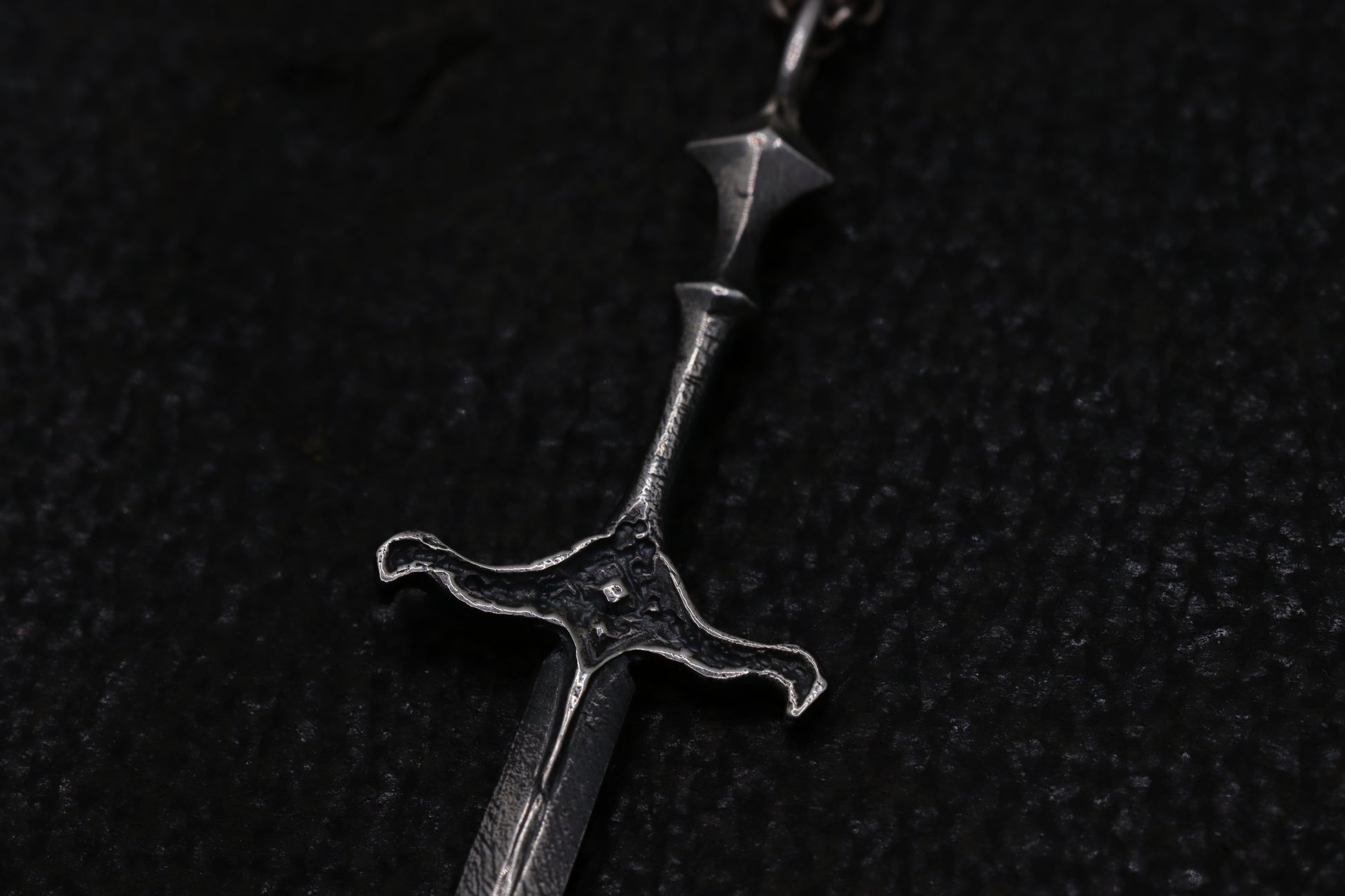 Close-up of a silver sword pendant on a dark textured background