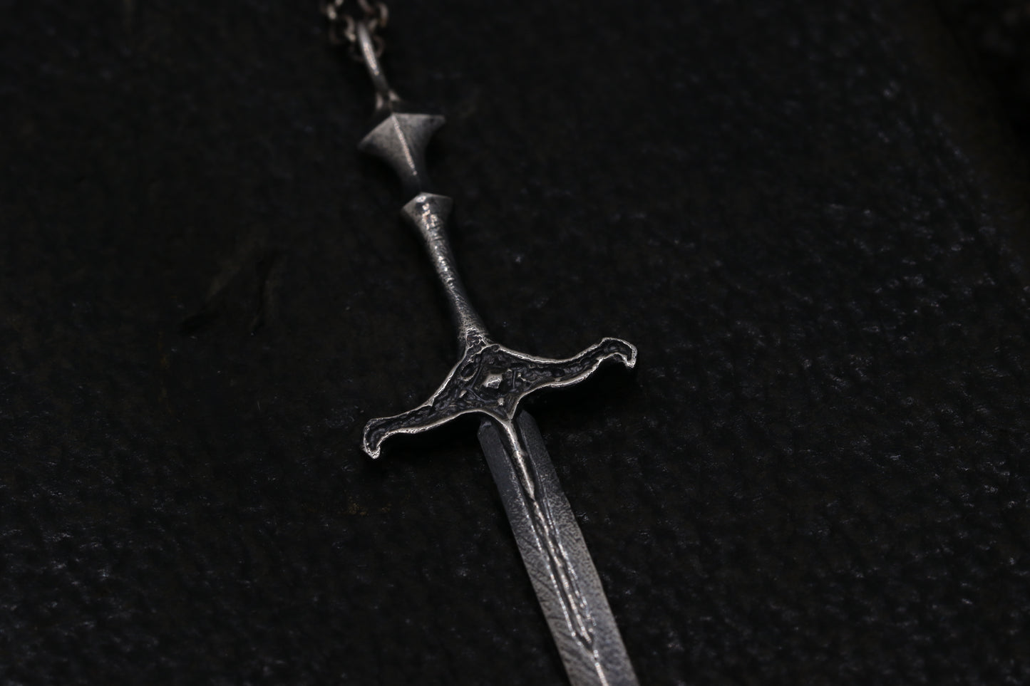 Silver sword-shaped pendant on a dark background