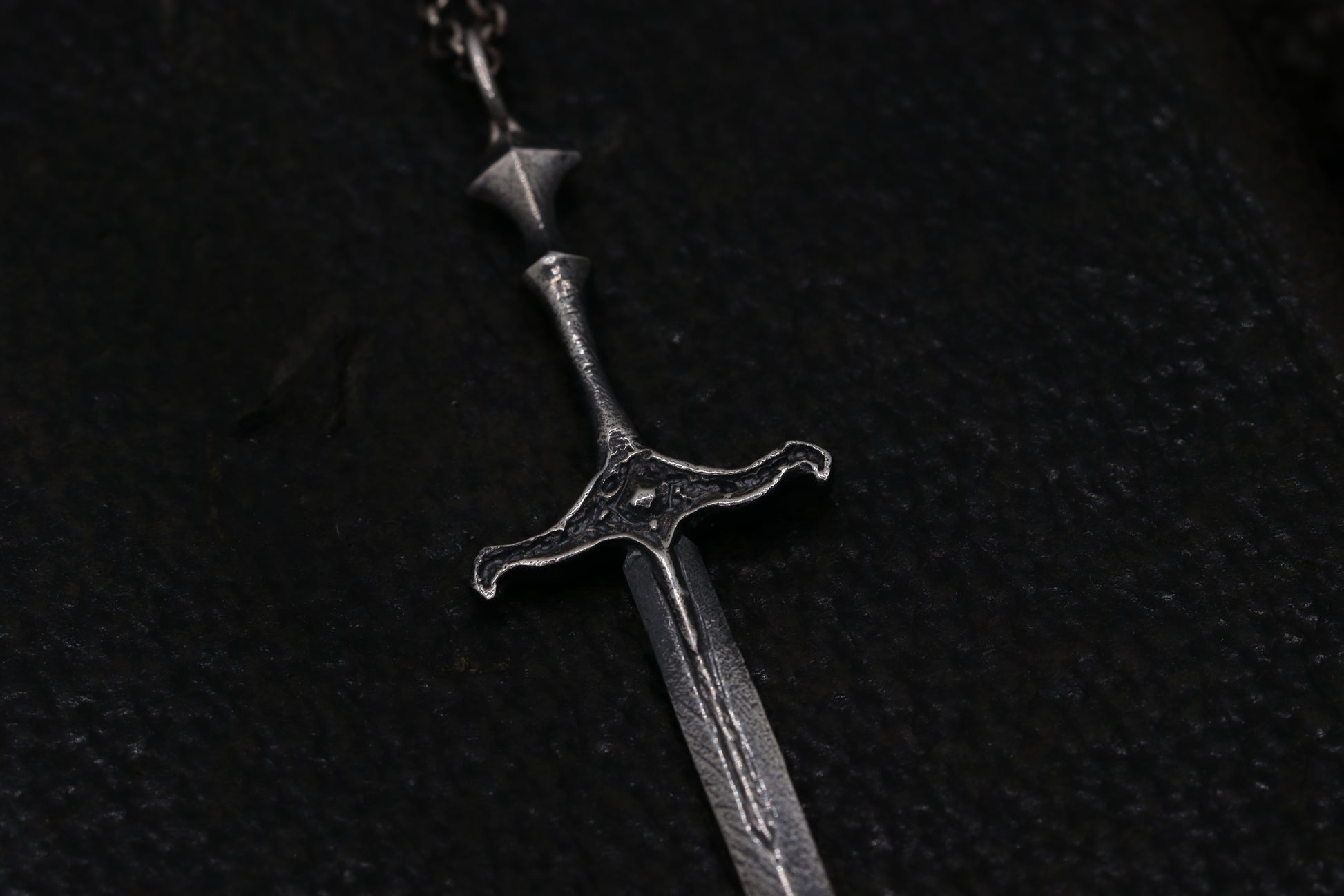 Silver sword-shaped pendant on a dark background