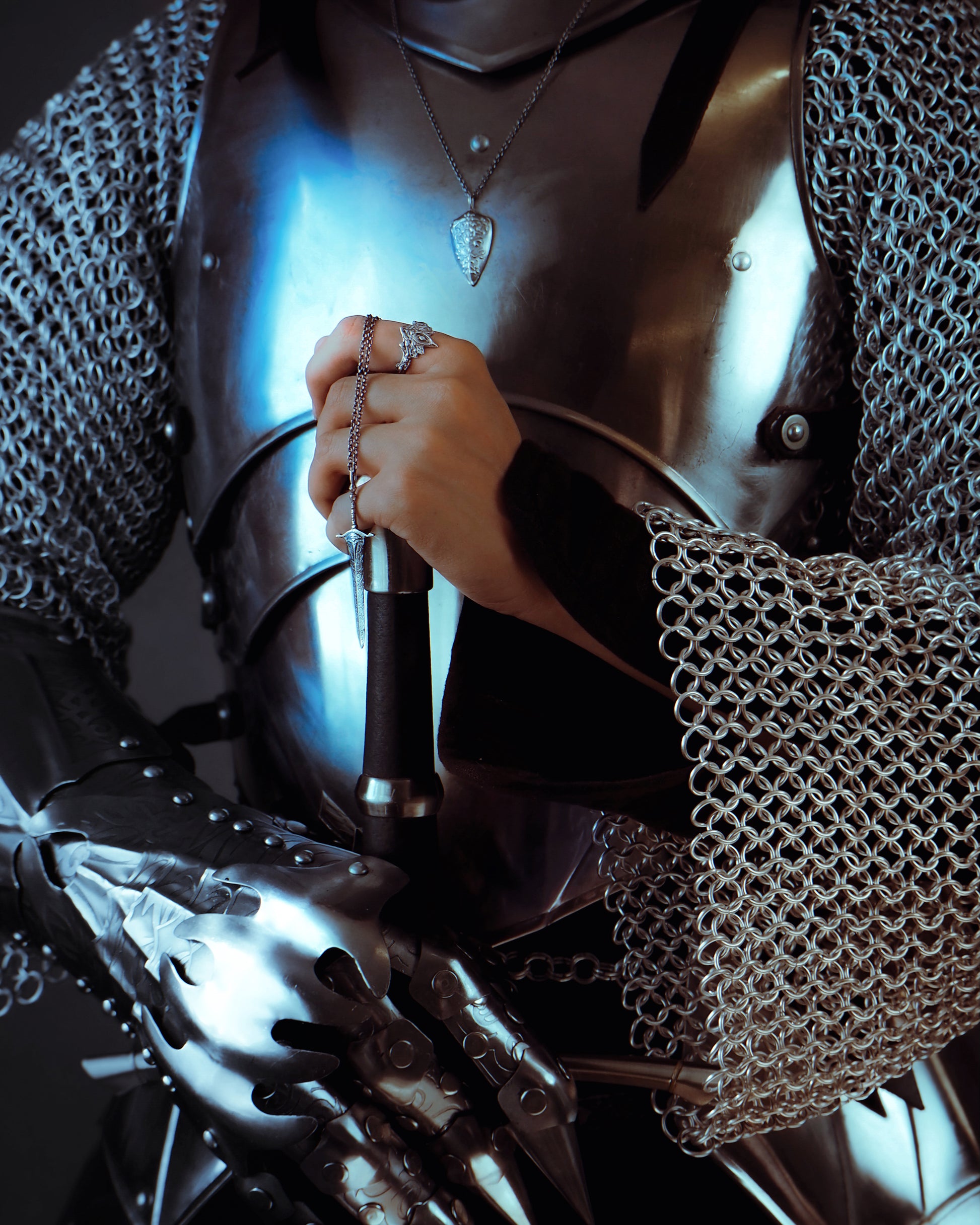Person in chainmail holding a sword with a dark background