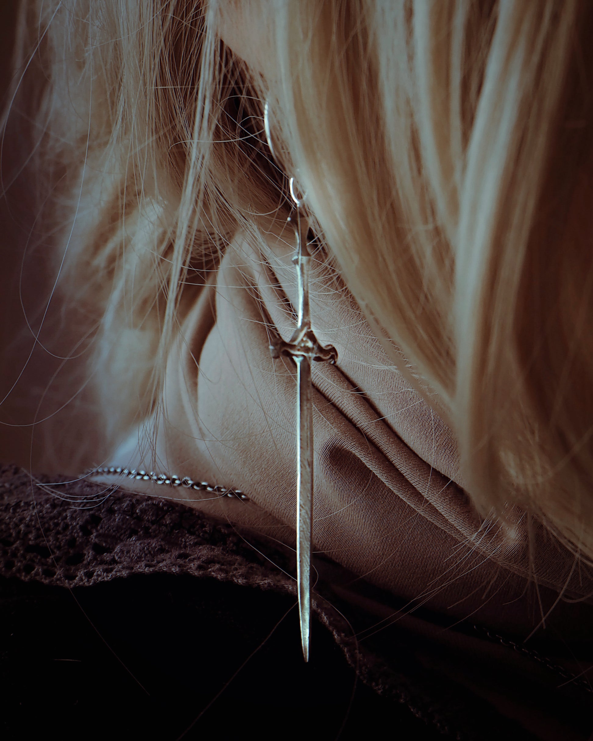 Close-up of a delicate silver earring with a sword design worn by a person with blonde hair.