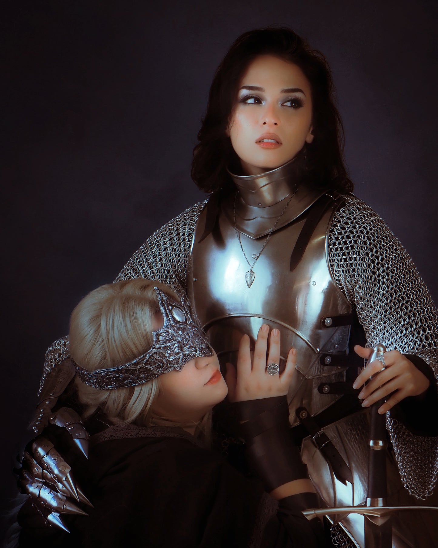 Woman in chainmail holding a sword with another person in the background