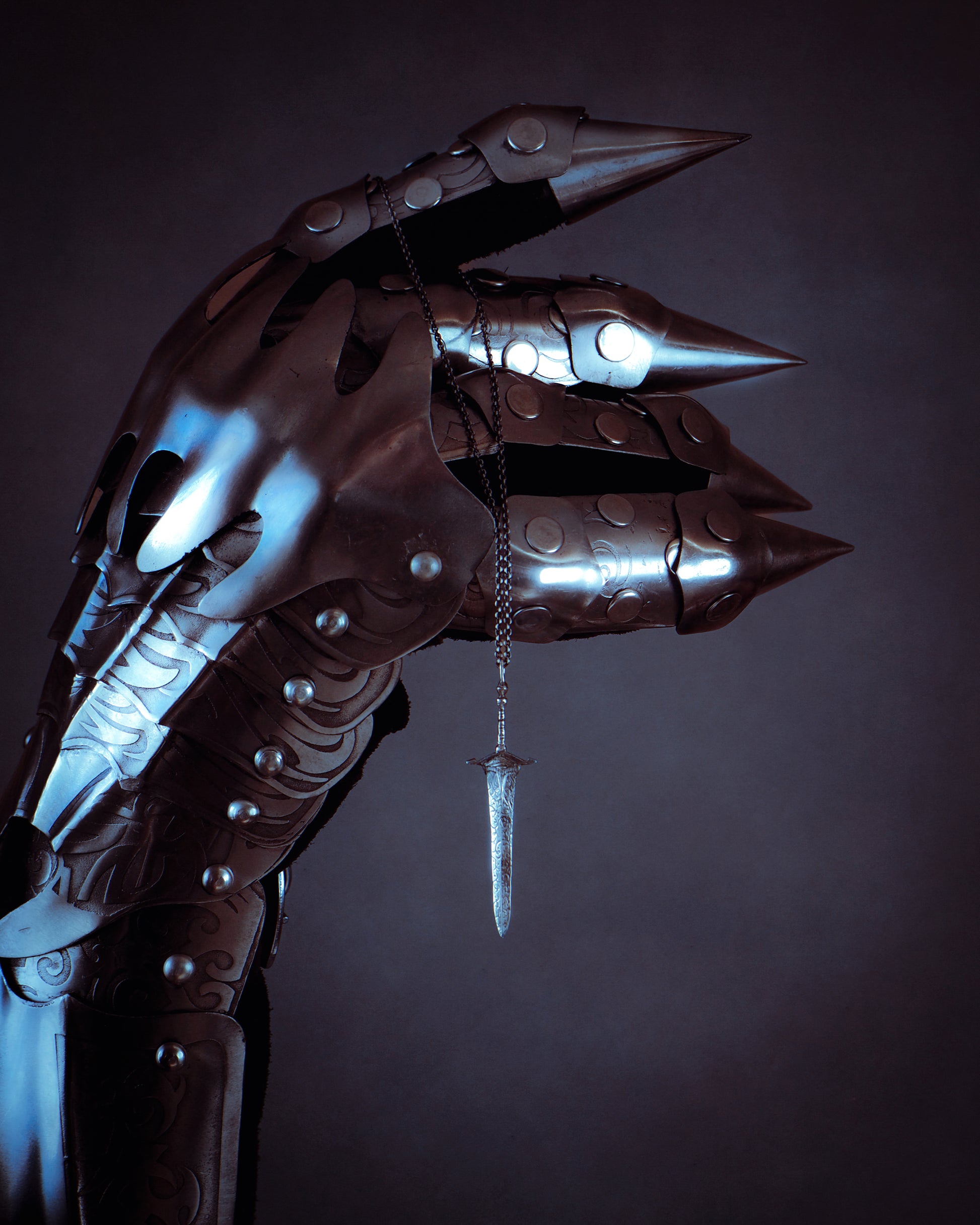 Close-up of a metallic dragon scale glove holding a sword-shaped necklace with a dark background