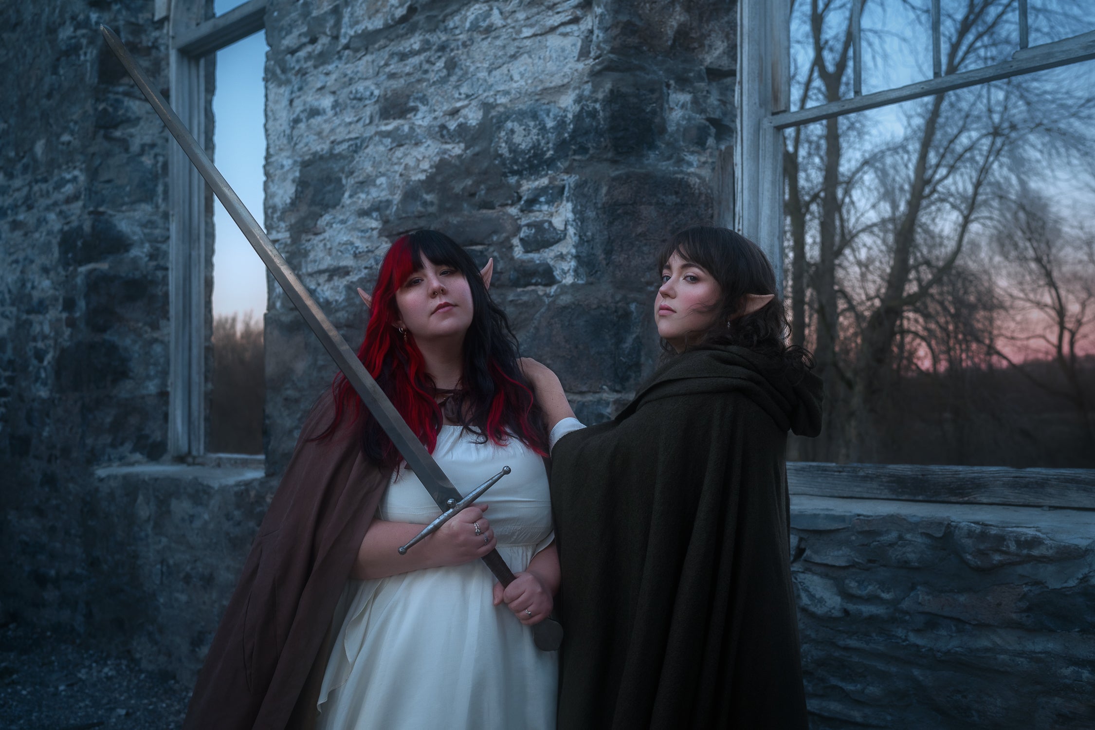 Two woman in a fantasy medieval setting looking at the camera, a sword in hands.