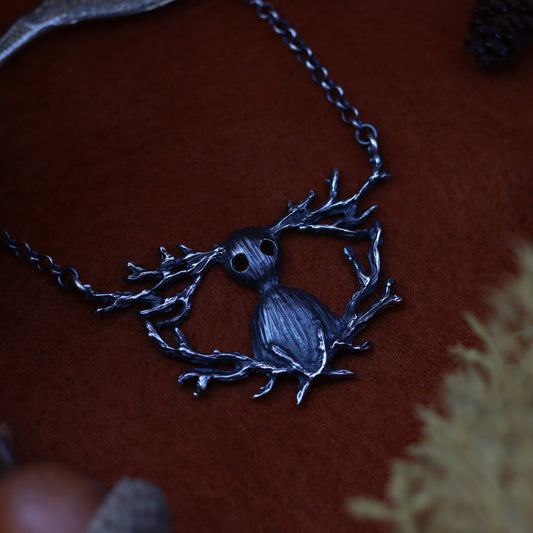A Sterling silver necklace with a unique design, featuring a character inspired by 'Over The Garden Wall' placed on a red surface with autumn leaves around it.