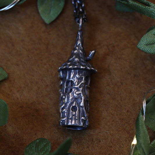 A hand-sculpted pendant necklace inspired by the Wizard's Tower from Stardew Valley, featuring intricate details and placed on a leafy background.