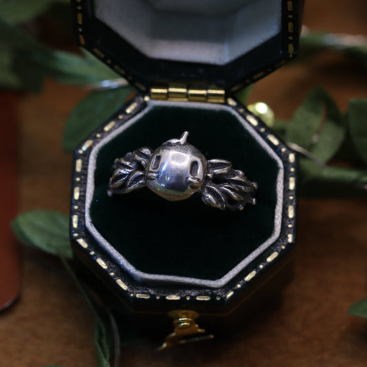 A hand-sculpted and cast metal pendant depicting a forest spirit, presented in a black octagonal box with a green velvet interior.