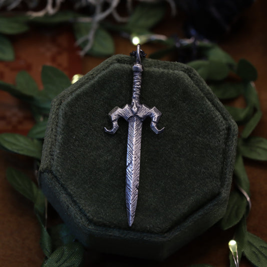 A necklace pendant designed to resemble the Galaxy Sword from the video game Stardew Valley, displayed on a dark, fabric-wrapped stand.
