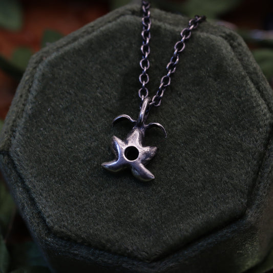 A sterling silver pendant necklace with a star-shaped fruit design, displayed on a gray cushion.