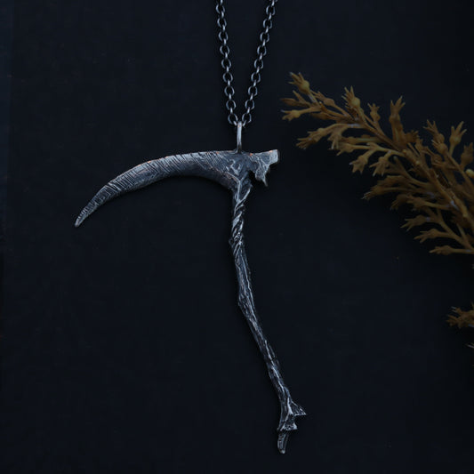 Grim Reaper-style pendant on a dark background with decorative elements