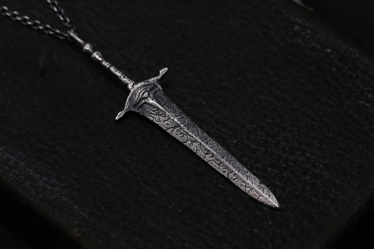 silver sword-shaped pendant on a dark fabric background