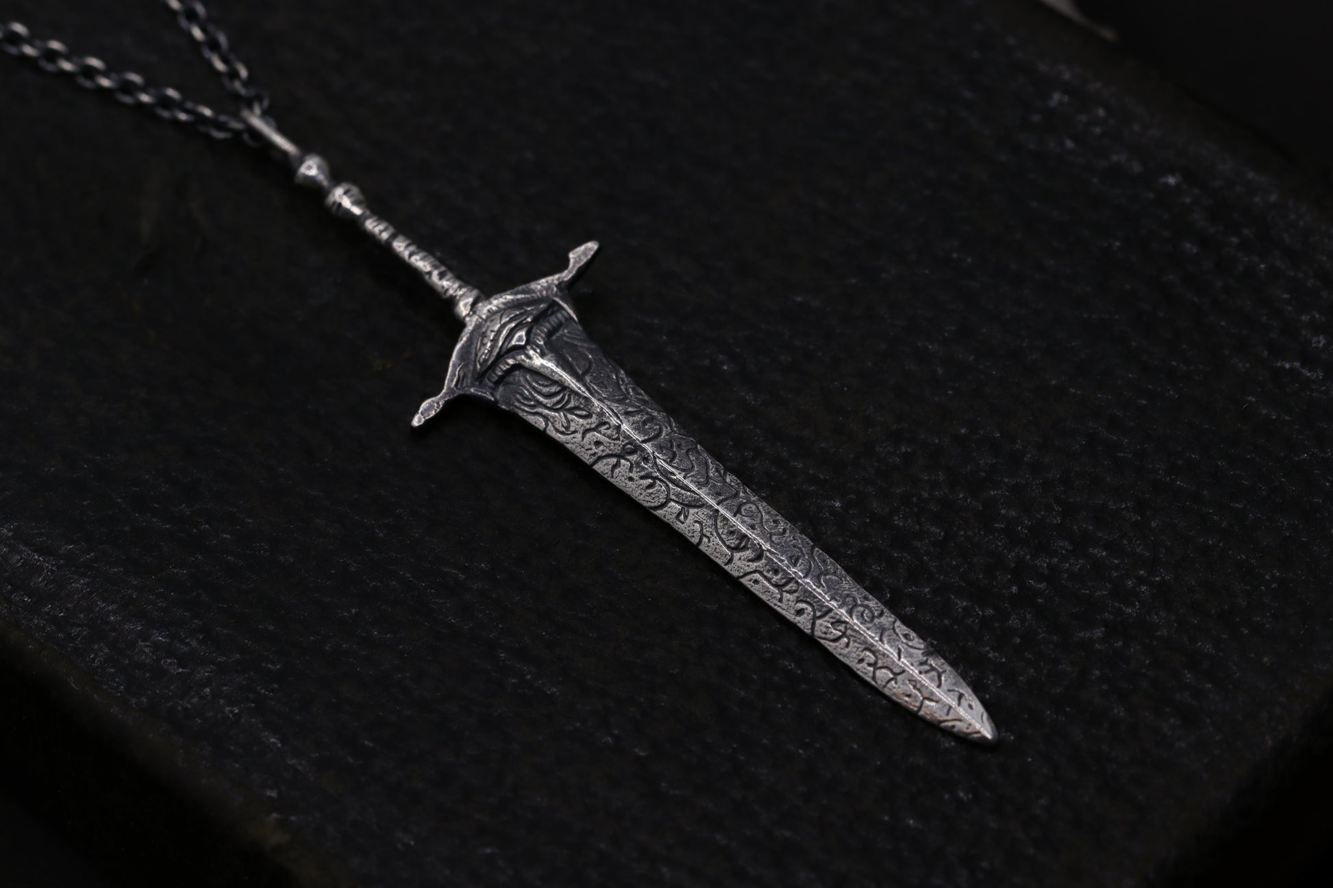 silver sword-shaped pendant on a dark fabric background