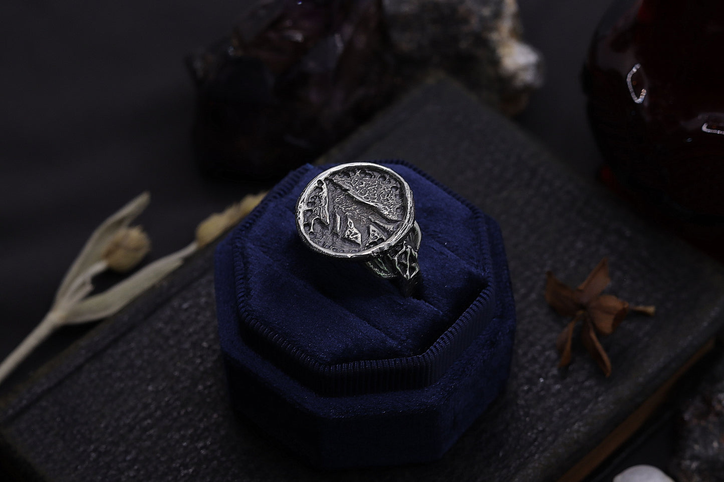 Silver wolf ring design on a blue velvet cushion against a dark background