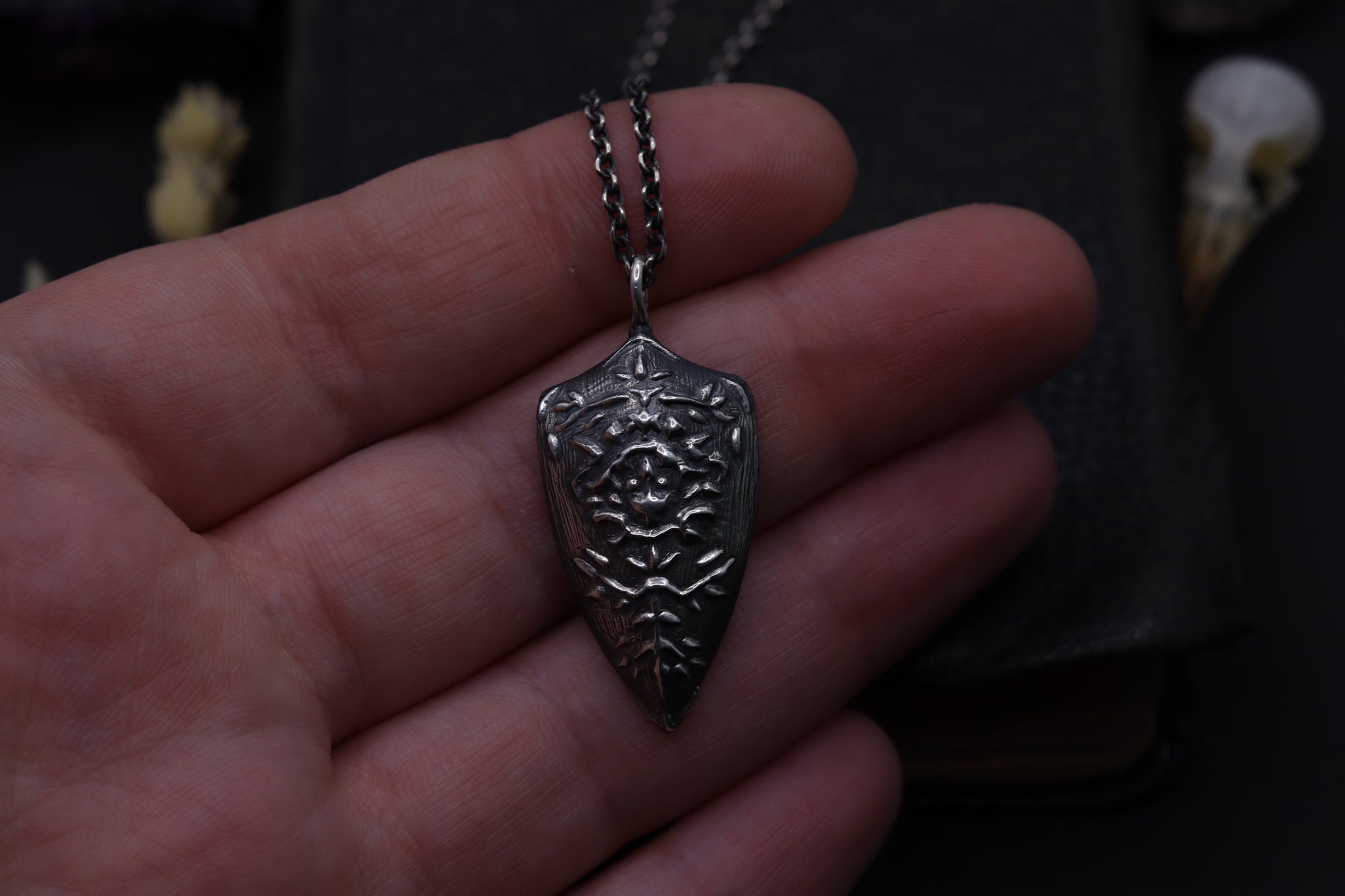Silver shield pendant on a chain held in a hand with a dark background