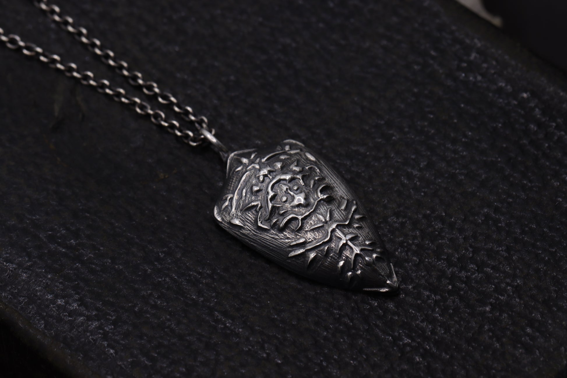 Silver shield-shaped pendant necklace on a black textured background