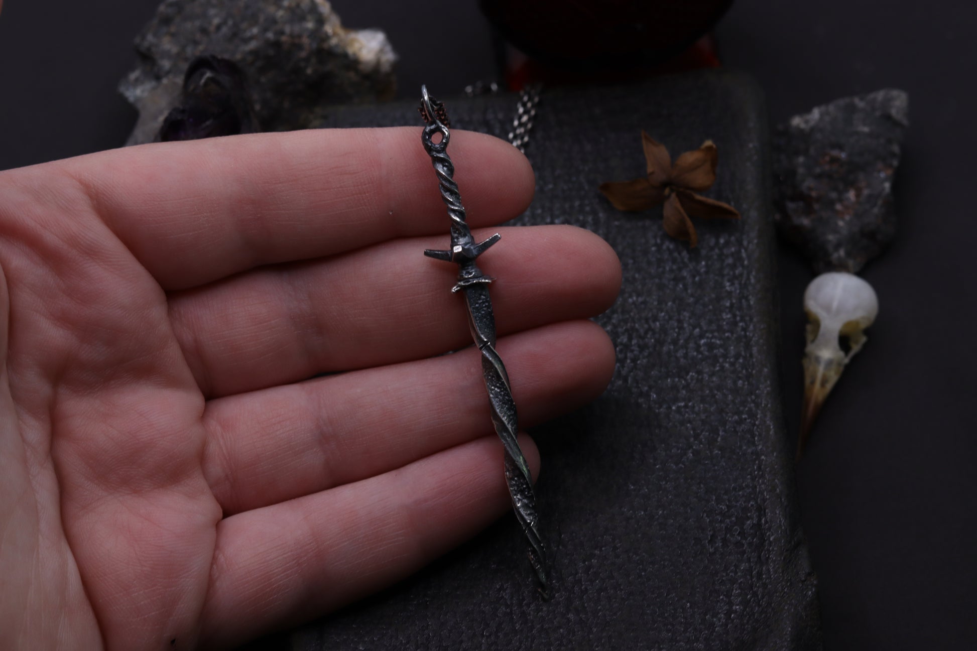 Hand holding a detailed silver sword pendant with a dark background