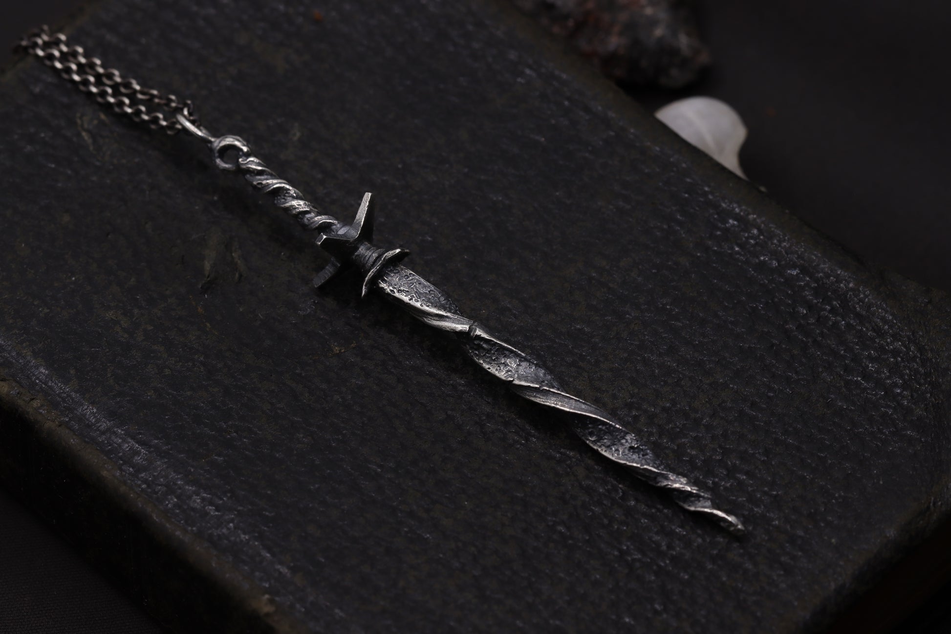 Silver sword-shaped necklace on a dark textured surface